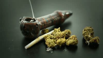 A smoking pipe, a rolled joint, and cannabis buds on a dark surface.