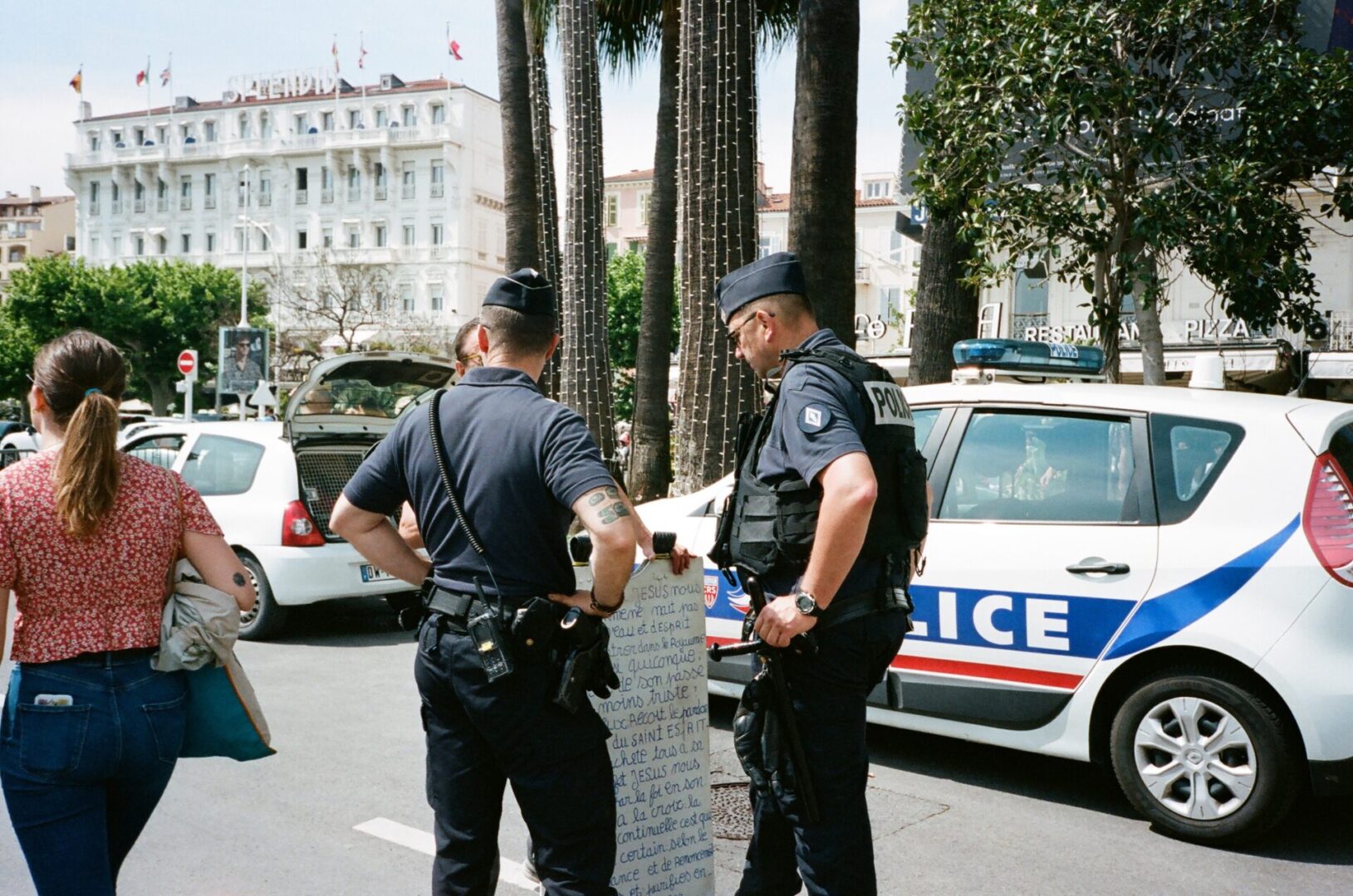 Two police officers talk to a person holding a handwritten sign near a police car.