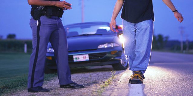 Two men with a car and its headlights on in the background.